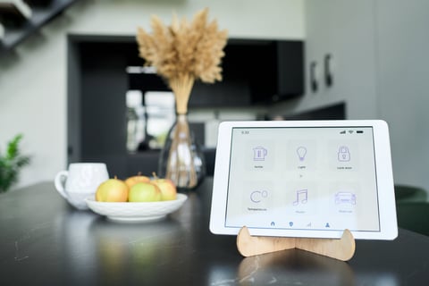 Home automation control tablet situated on kitchen counter surrounded by fresh apples in bowl and dried flowers in vase