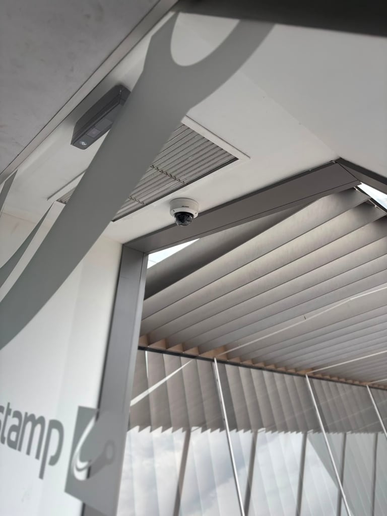Overhead view of a modern pergola or awning with white metal louvers, adjustable ceiling vents, and a dark frame