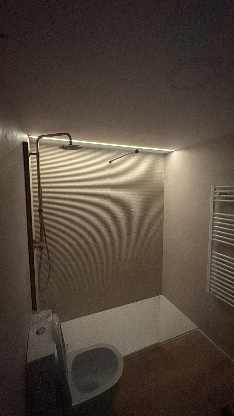 Modern bathroom with white toilet, shower enclosure with glass panel, heated towel rack, and LED strip lighting on ceiling