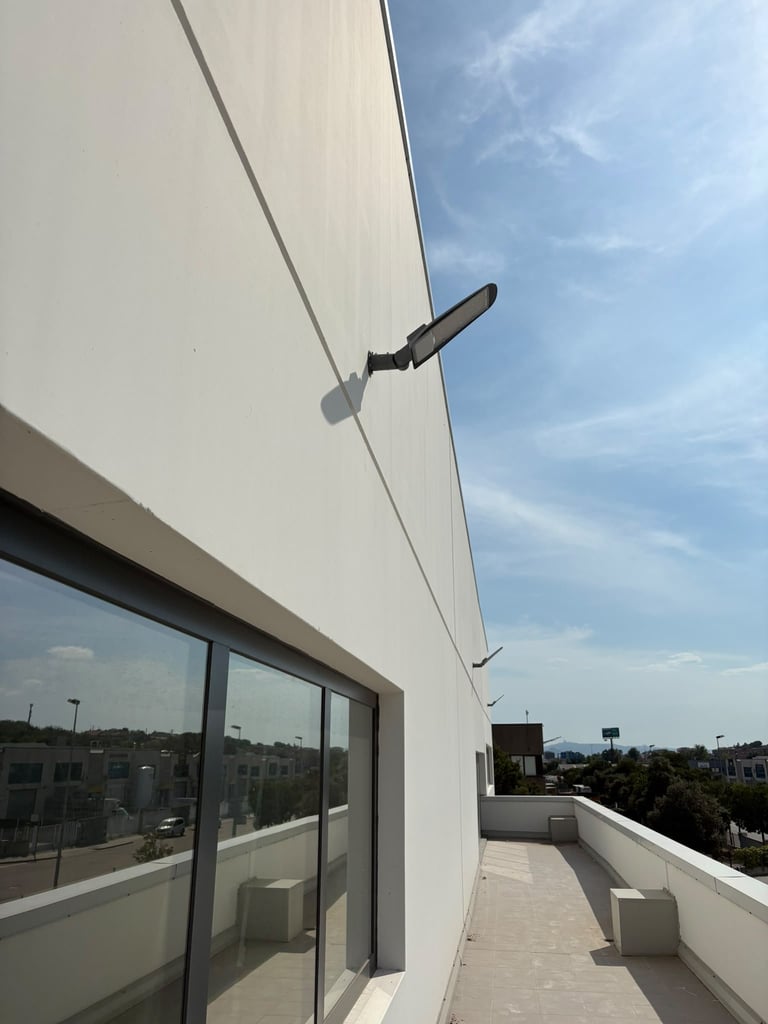 Modern rooftop terrace with white walls, large windows, and an adjustable awning mounted above, overlooking a residential area under blue sky